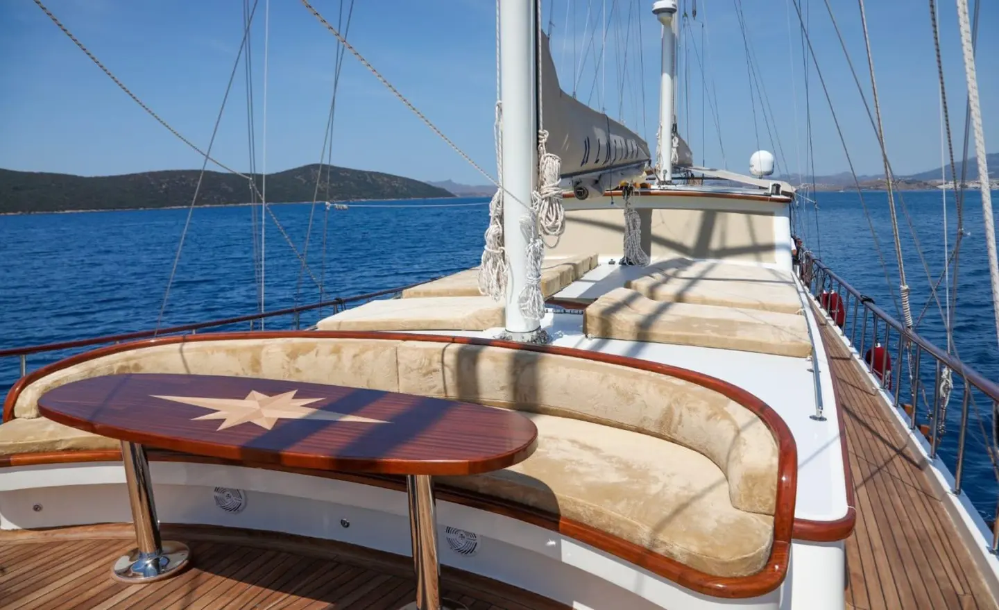 Ulucinar yacht deck with cushioned seating, wooden table, and sea view at sunset