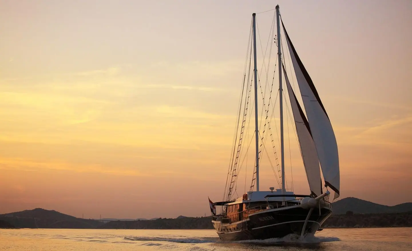 Aurum gulet yacht sailing at sunset on calm water with distant hills