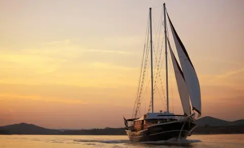 Aurum gulet yacht sailing at sunset on calm water with distant hills
