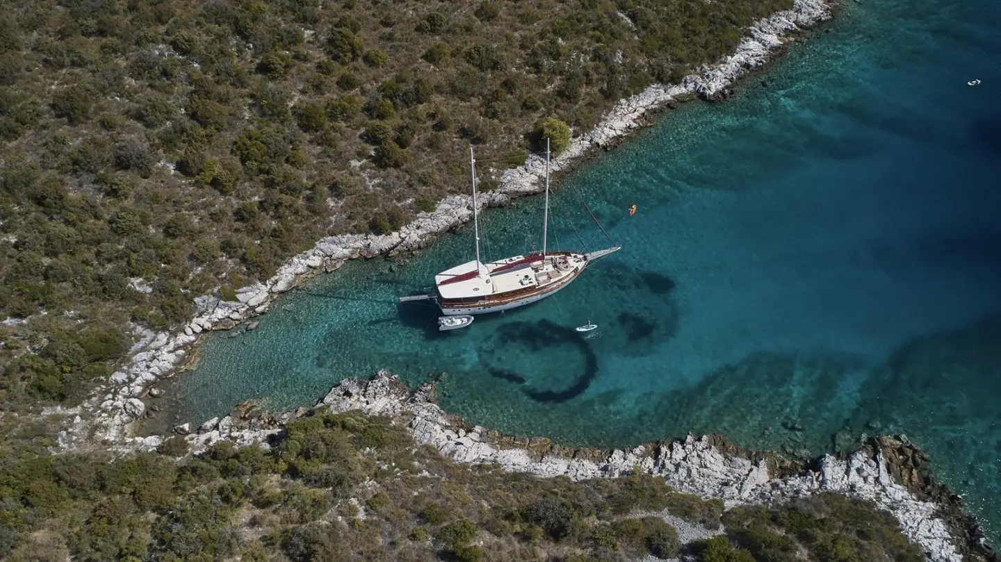 A white yacht anchored near rocky coastline under clear blue water and sky