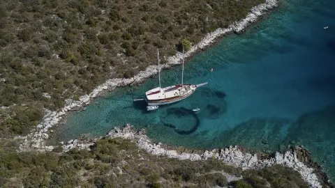 A white yacht anchored near rocky coastline under clear blue water and sky