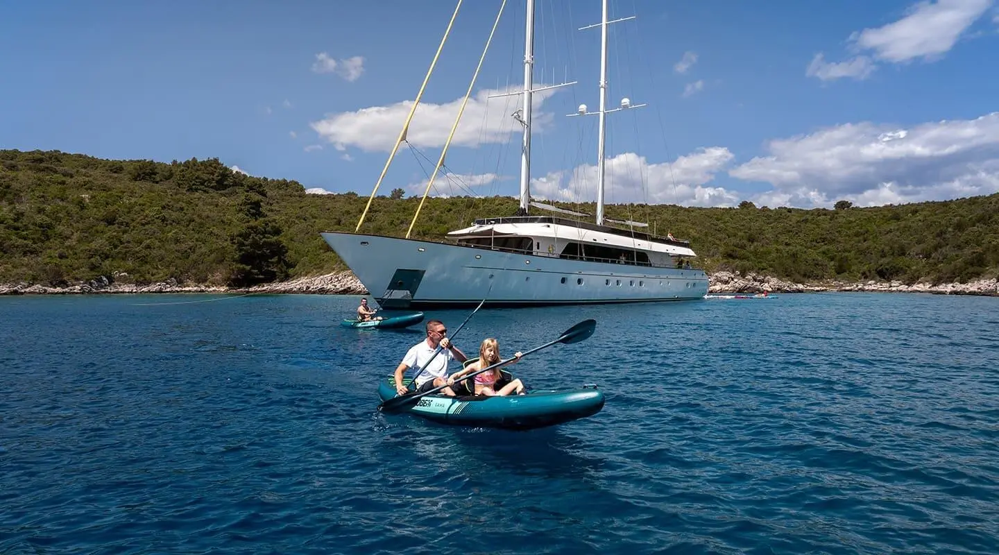 Small motorboat with two people in blue water near a luxury yacht Anima Maris anchored
