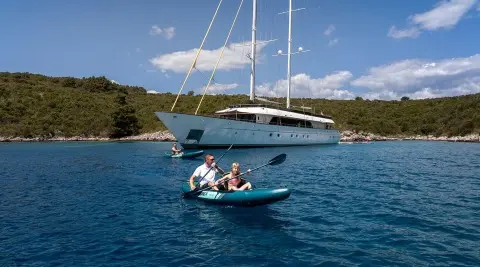 Small motorboat with two people in blue water near a luxury yacht Anima Maris anchored