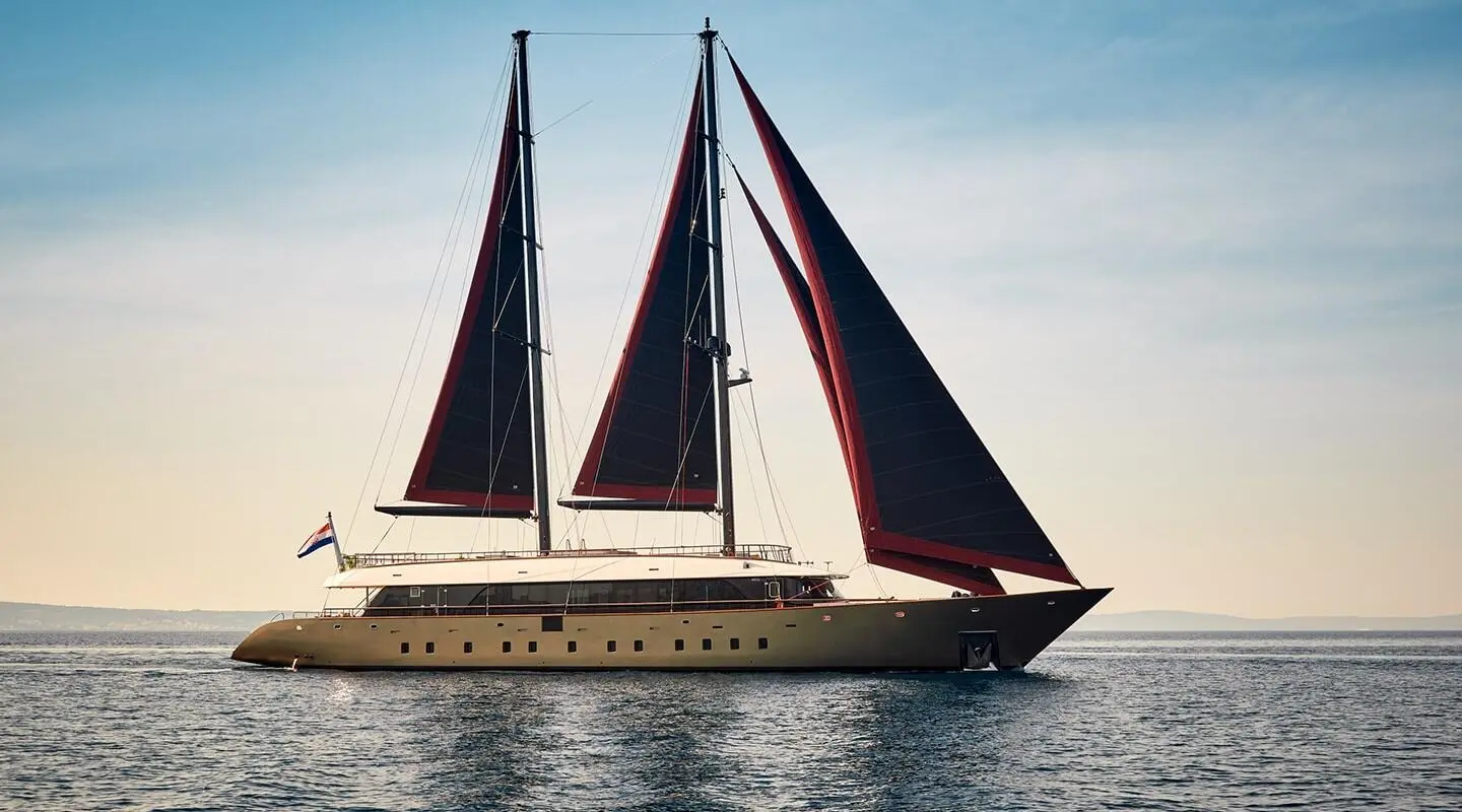 Yacht Anetta sailing with black and red sails on calm blue water
