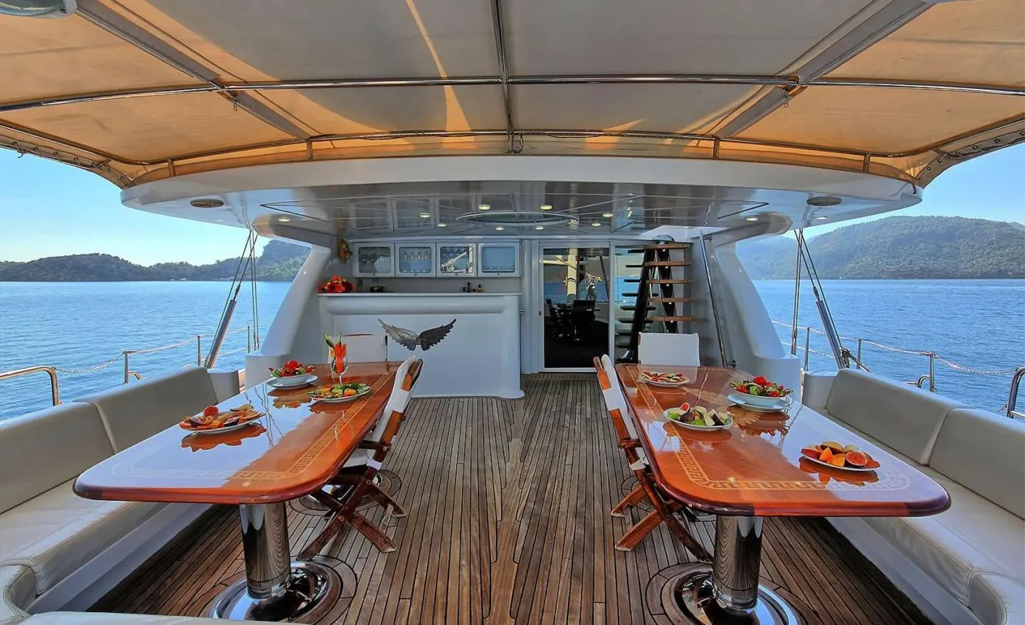 Angelo II yacht interior deck with wooden dining tables and chairs at sunset