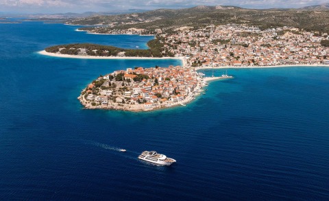Small island with red-roofed houses along a coastal town and blue sea surrounding a yacht