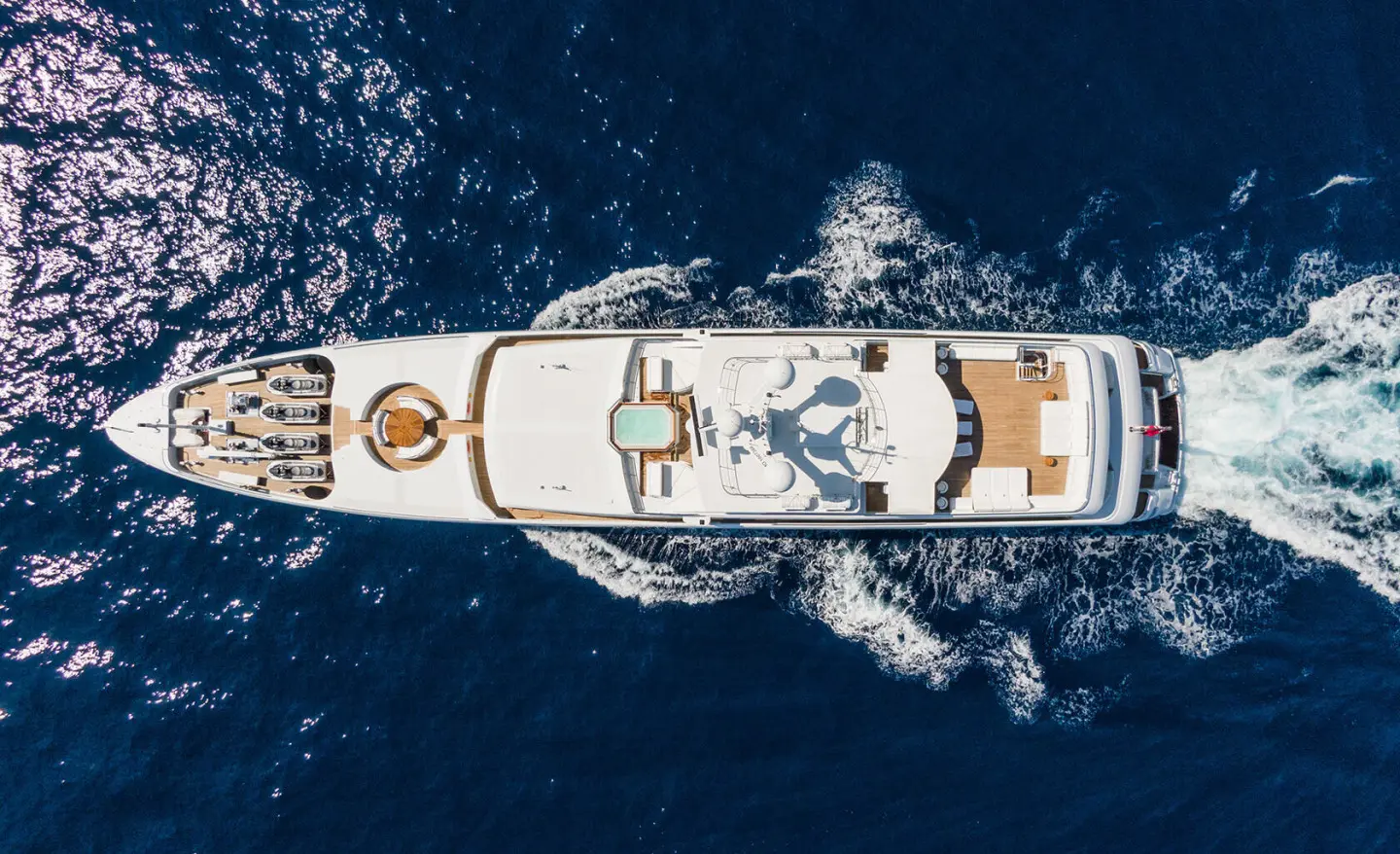 Top-down view of Apogee yacht cutting through blue sea, wake visible