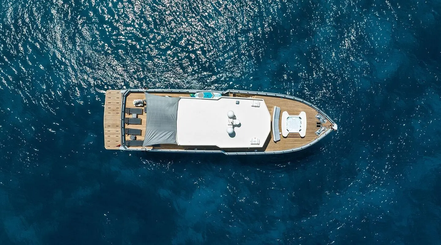 A luxury yacht shown from above cruising in blue sea with deck and sunbed area