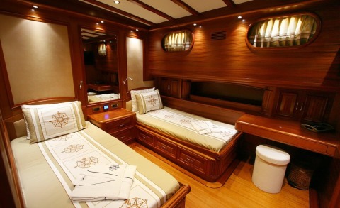 Wooden-paneled yacht interior with two twin beds, pillows, and built-in cabinets