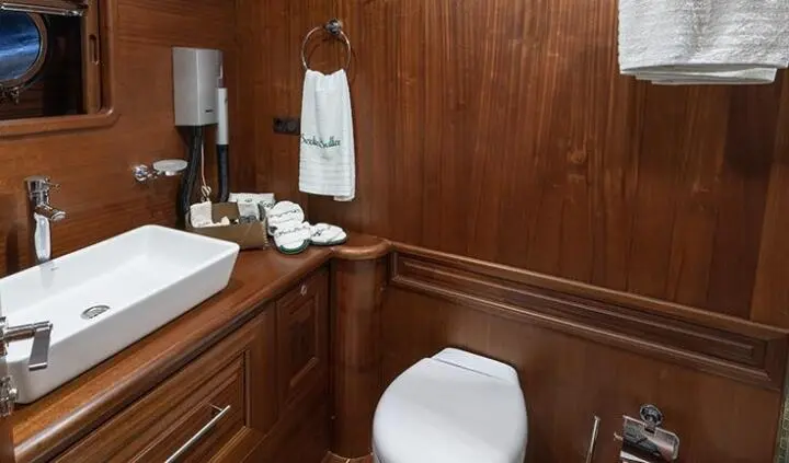 Opulent yacht cabin with wooden paneling, white bed sheets, and ensuite bathroom