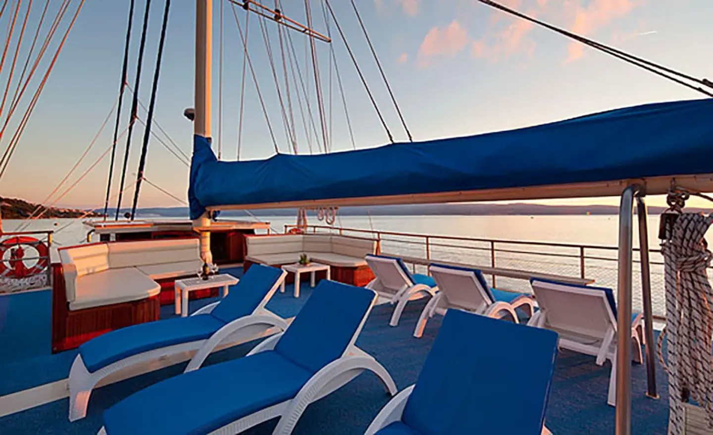 Sun loungers with blue cushions on a luxury sailing yacht deck at sunset
