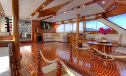 Angelo II interior: luxurious 35m yacht salon with polished wood floors, cream upholstery, and a round glass table with pink flowers