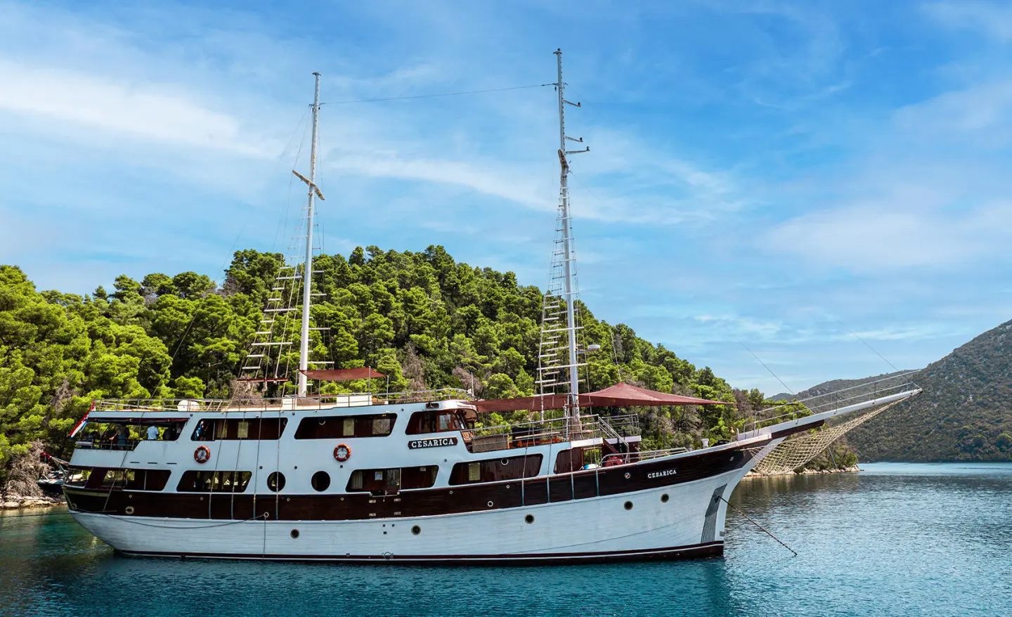 Cesarica luxury sailing yacht anchored with blue sky and green hilly backdrop