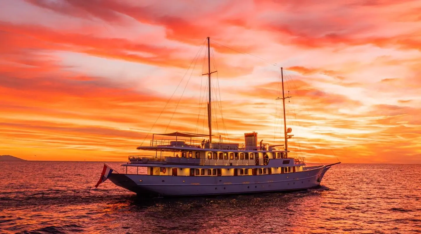 Bellezza luxury yacht silhouetted at sunset with warm orange sky