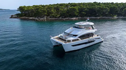 Luxury motor yacht named By My Side docked in calm blue water near a tree-lined shore