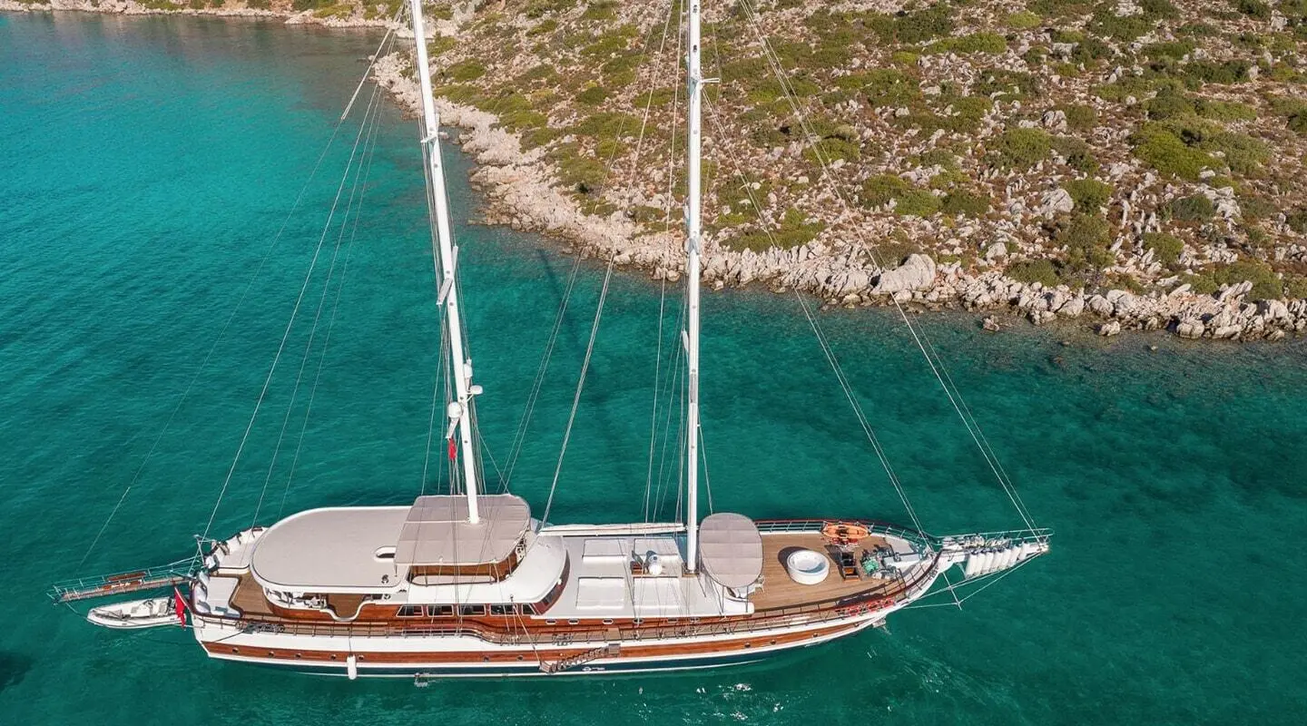 Halcon Del Mar sailing yacht anchored near shore at sunset with teal water