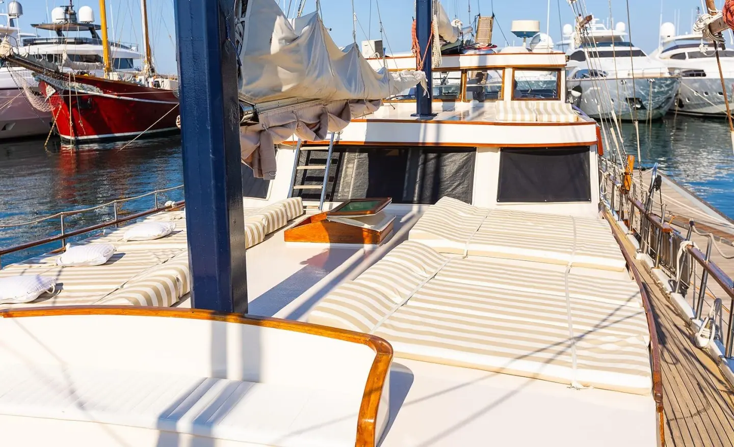 Sun loungers with striped cushions on an open deck, other yachts in the marina visible
