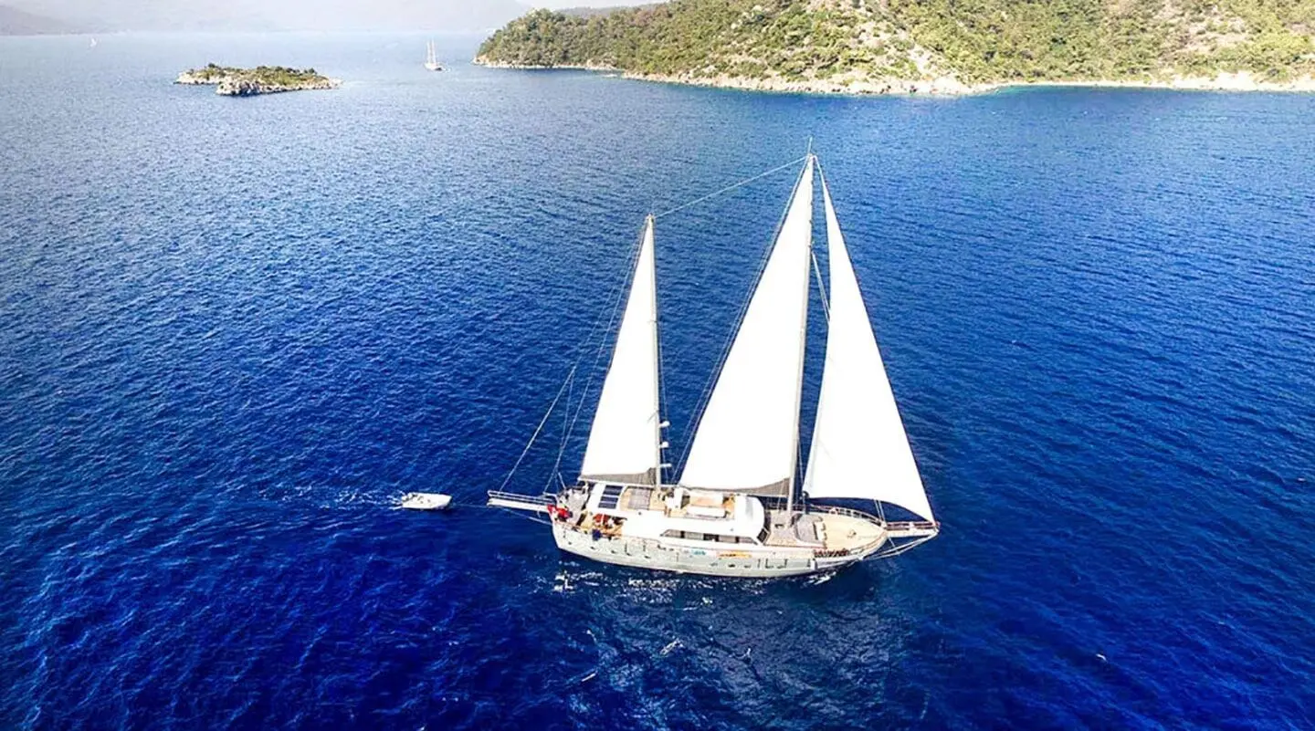 Gulet Virtuoso sails on deep blue sea near rocky coastline, clear sky