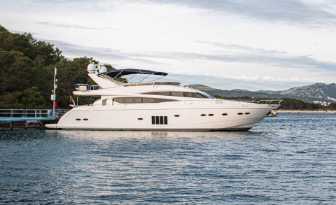 White motor yacht docked at the pier with trees and coastline in the background
