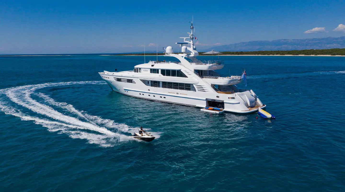 Alalya luxury motor yacht cruising blue sea with wake and small boat nearby