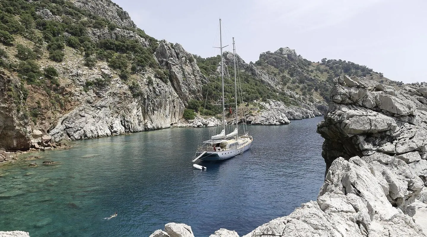 Sailing yacht anchored in a secluded cove with rocky cliffs at sunset
