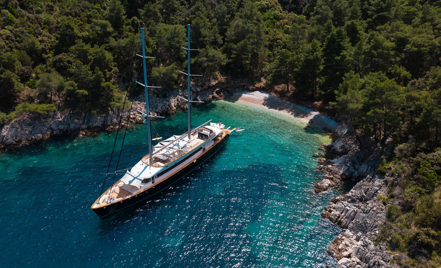 Dalmatino yacht anchored near rocky coastline with clear blue water