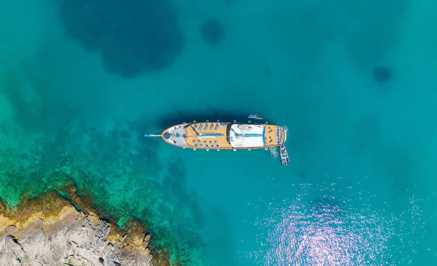 A white luxury gulet yacht named Mendula sails clear turquoise water near rocky coastline at sunset