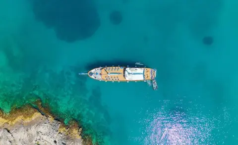A white luxury gulet yacht named Mendula sails clear turquoise water near rocky coastline at sunset