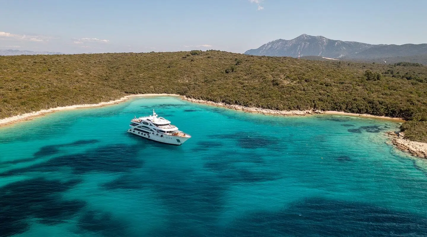 White motor yacht anchored in turquoise water near a rocky coastline