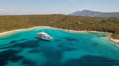 White motor yacht anchored in turquoise water near a rocky coastline