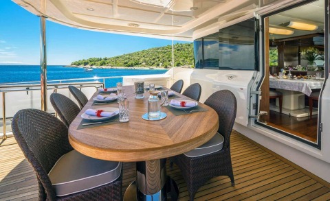 On the exterior deck, a large wooden table with chairs and sea view; interior door to the cabin visible