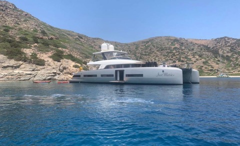 White motor yacht Just Marie 2 anchored on calm blue water with rocky shore in the background