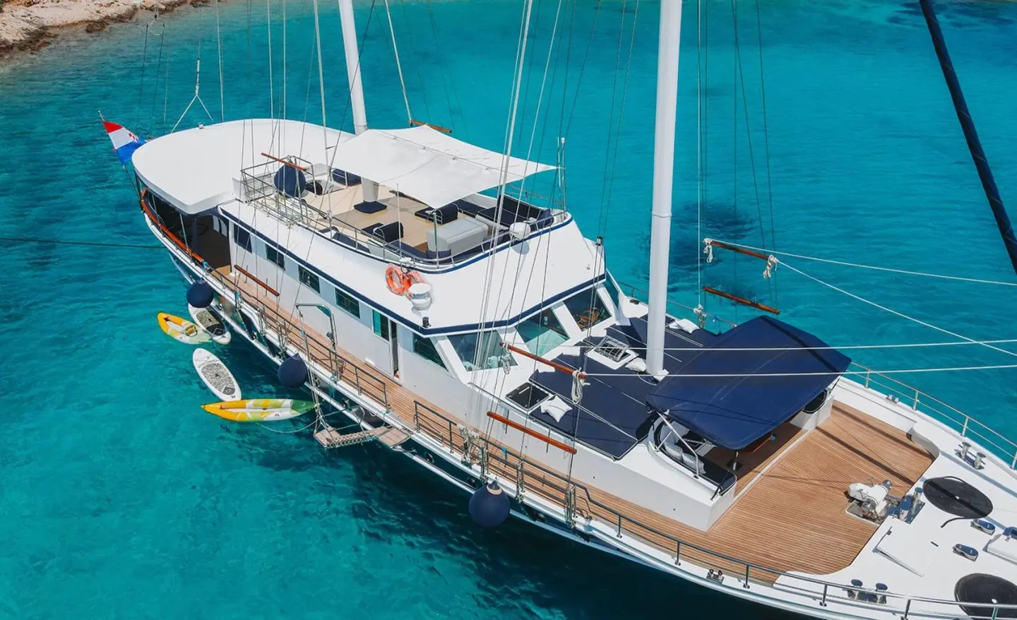 Aurum luxury yacht anchored in turquoise waters with deck lounge and sails visible