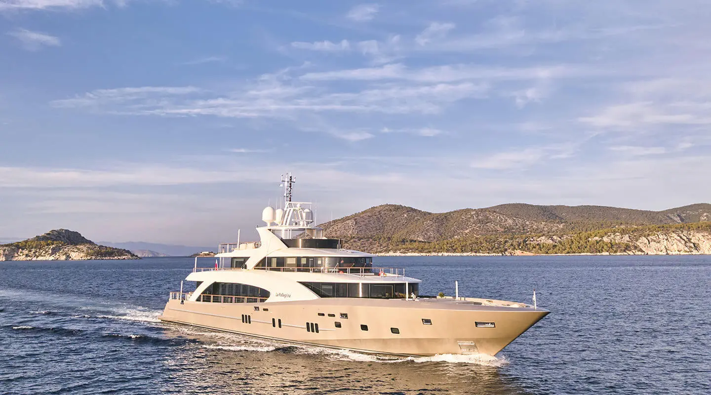 Luxury yacht La Pellegrina 1 moored on calm blue water with coastal hills behind