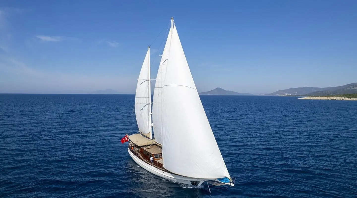 Arabella sailing yacht under full white sails on blue sea near coastline
