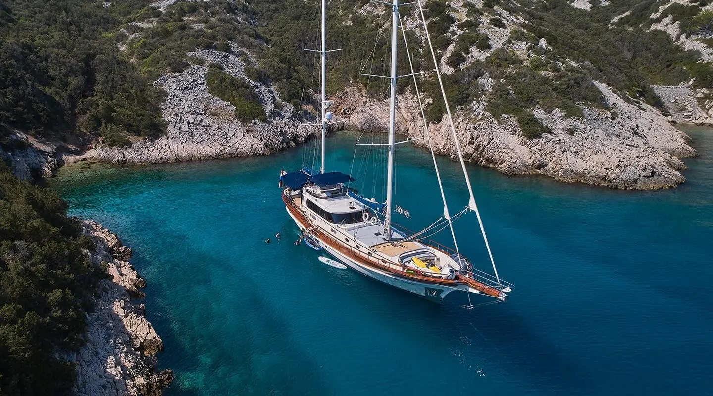 Sailing yacht anchored in a turquoise bay with rocky cliffs surrounding