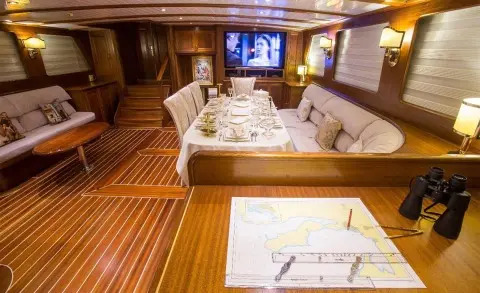 Interior of luxury gulet yacht Ece Berrak with wood deck, seating, and table setup at sunset