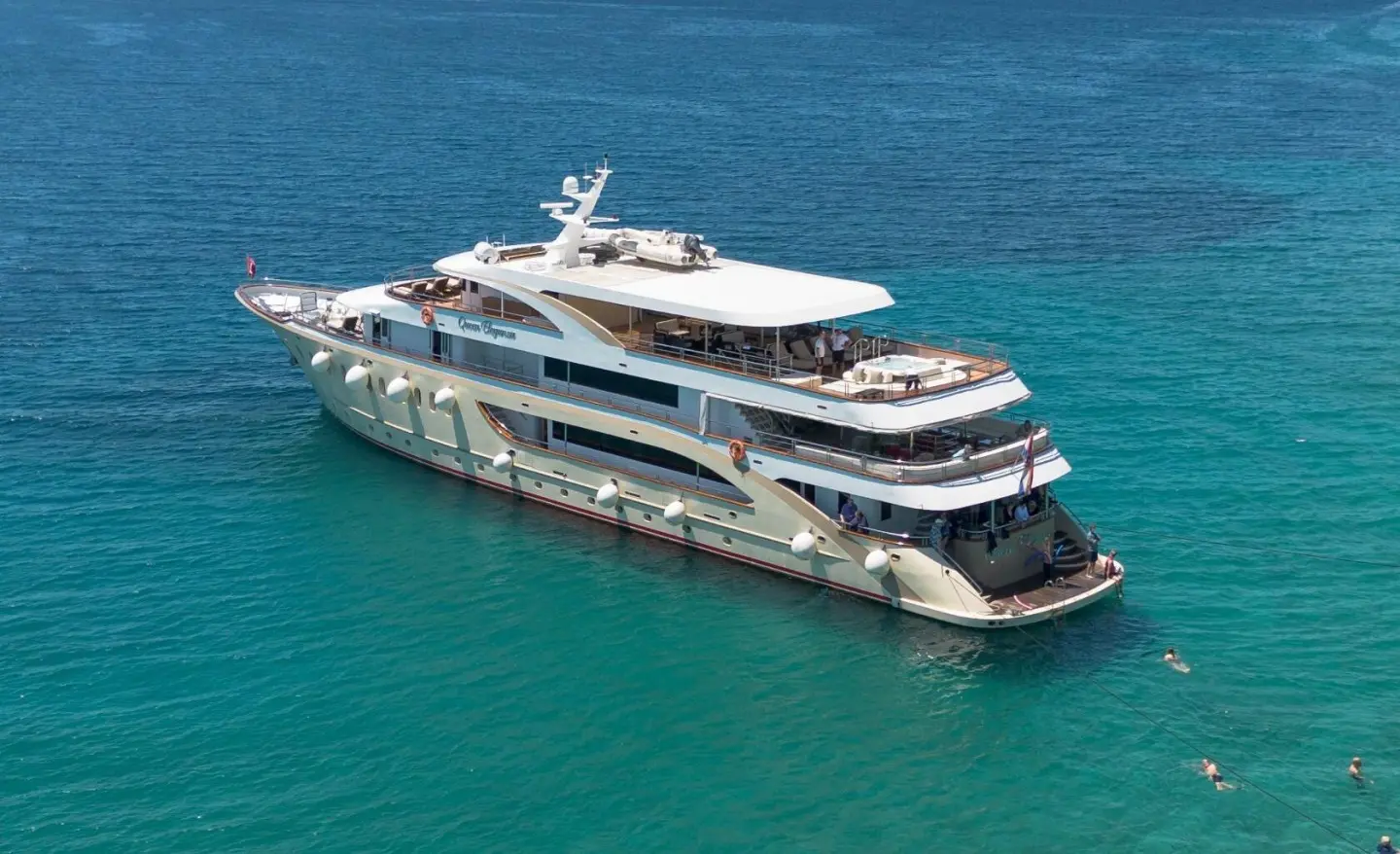 A multi-deck white yacht named Queen Eleganza anchored in blue-green sea