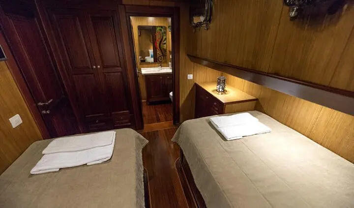 Twin cabins with beds, wood paneling, and a doorway between rooms on a yacht