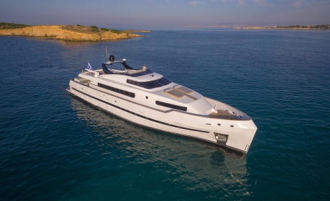 White luxury motor yacht anchored in blue sea with coastline in the background