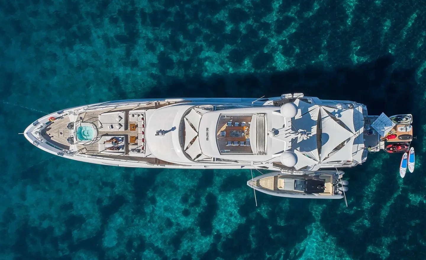 Top-down view of a sleek white luxury motor yacht named Happy Me anchored in turquoise waters