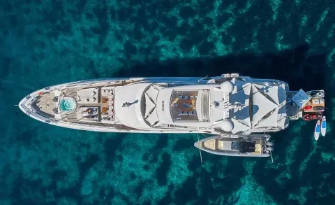 Top-down view of a sleek white luxury motor yacht named Happy Me anchored in turquoise waters