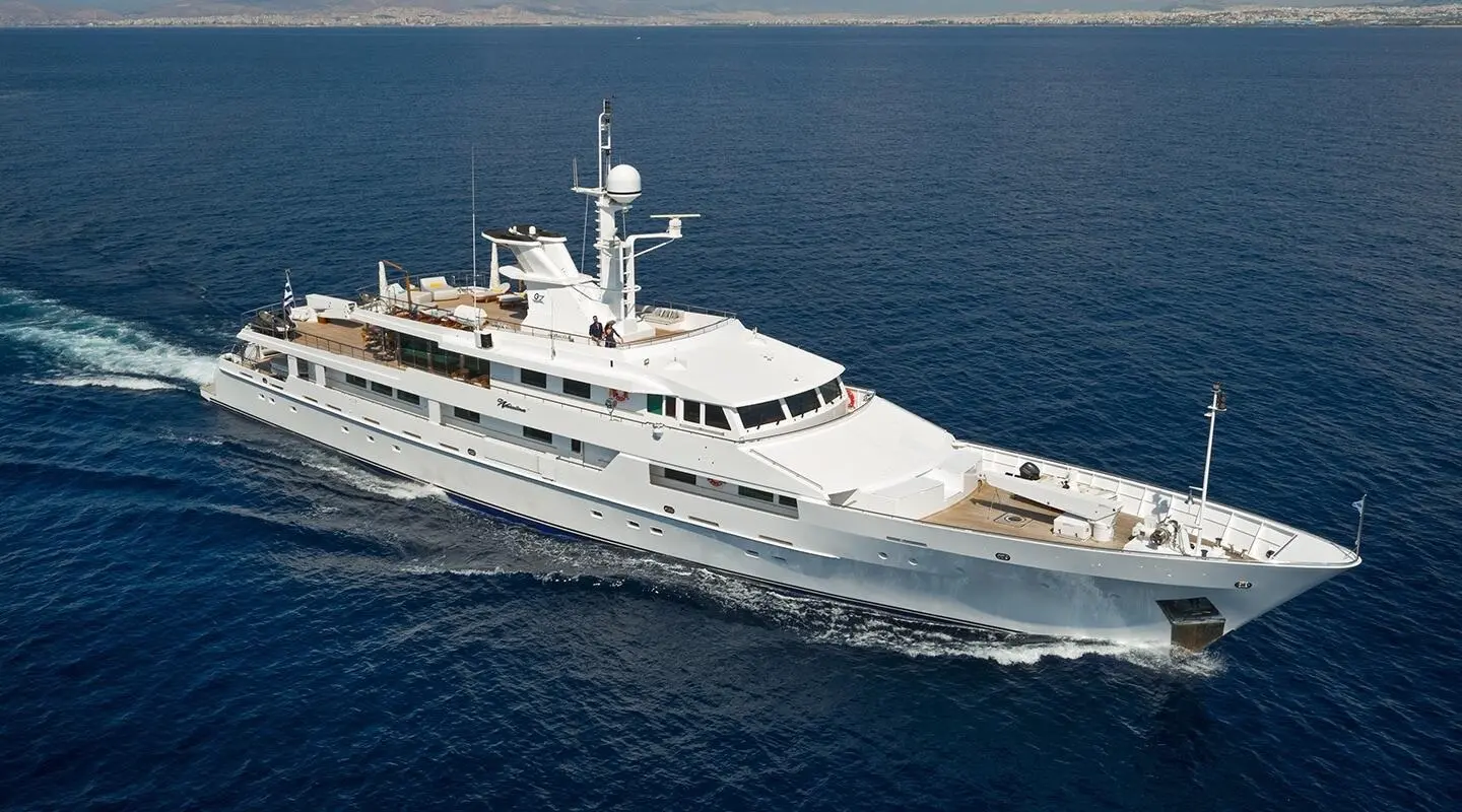 White yacht sailing in open sea with upper deck seating and masts visible
