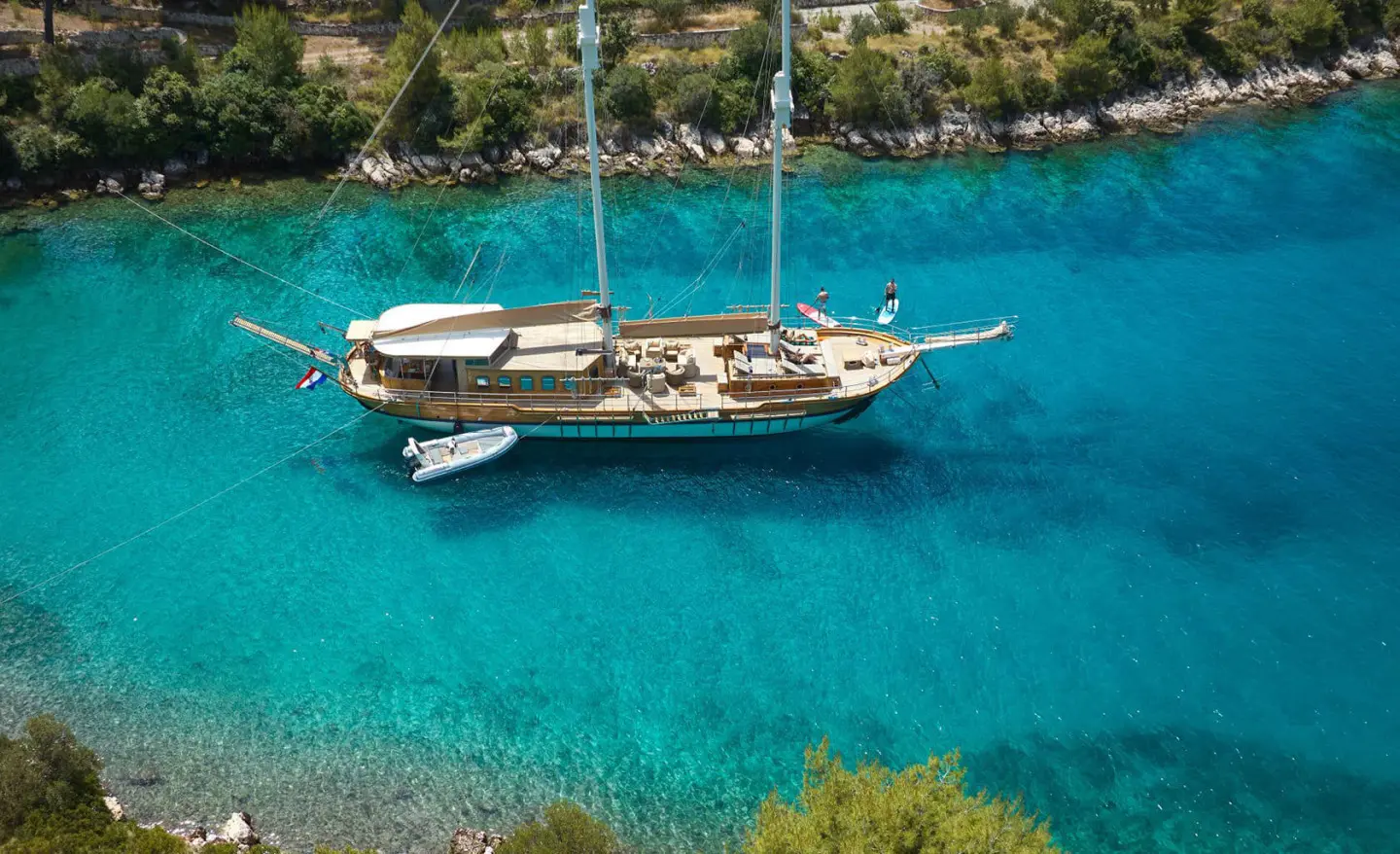 Luxurious sailing yacht Libra anchored in turquoise clear water near rocky coastline at sunset