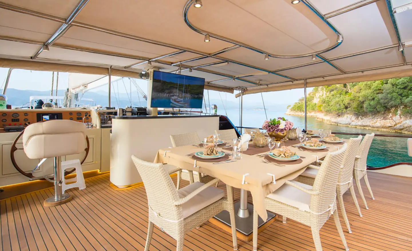 Sunlit yacht deck with beige seating, dining table and chairs under a canopy