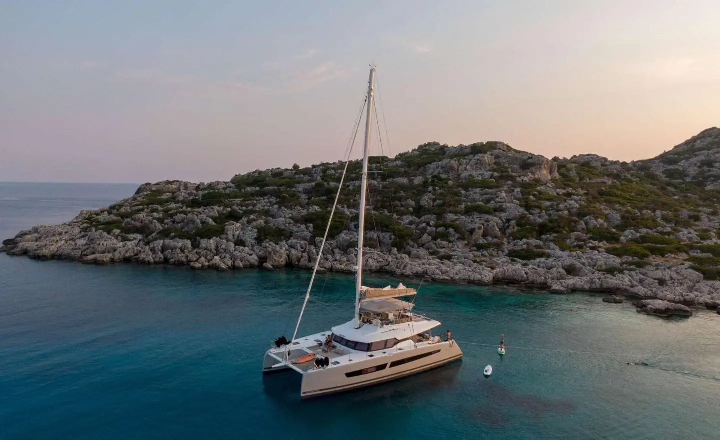 Serenissima luxury catamaran anchored near rocky coastline at sunset