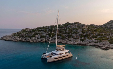 White luxury catamaran yacht anchored near rocky coastline at sea