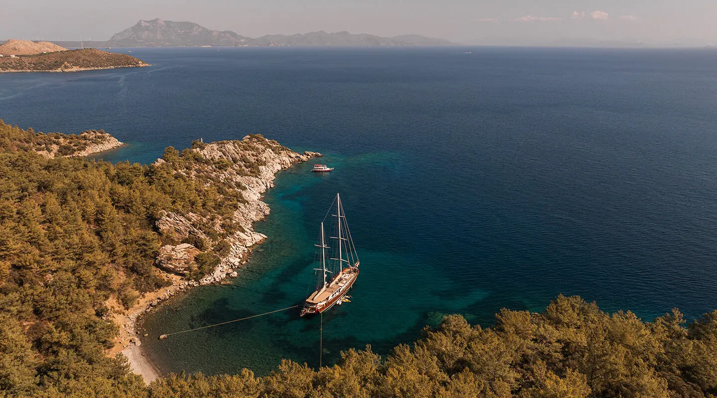 Overhead view of a luxury gulet anchored near rocky coastline at sunset