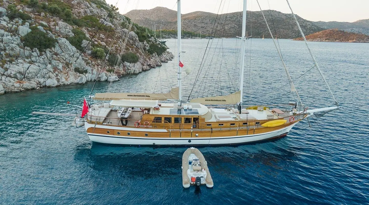 Small wooden gulet yacht Derin Deniz anchored near rocky shore with yellow hull