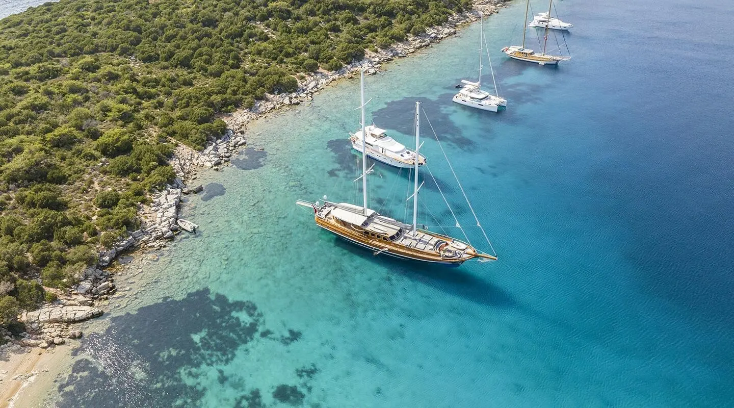 Gulet yacht Bedia Sultan anchored in turquoise clear water near rocky shoreline